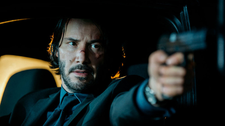 John Wick aiming a gun while sat in a car