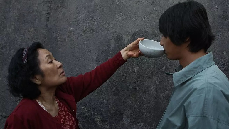 Mother giving Do-joon a drink from a bowl in "Mother" (2009)