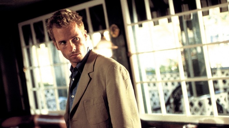 Leonard standing askew in a bar, wearing a tan suit and blue shirt, in Memento (2000)