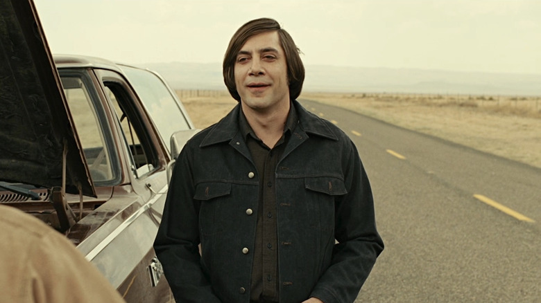 Anton Chigurh stands next to a car with its hood up in No Country for Old Men (2007)