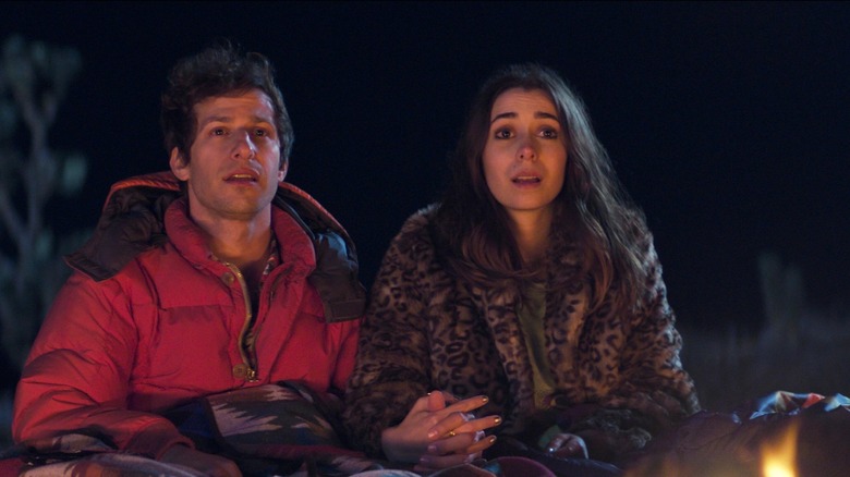 The two leads of Palm Springs holding hands by a campfire (2020)