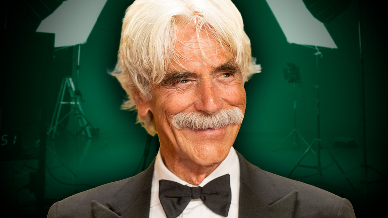 Sam Elliott smiling and wearing a tuxedo in front of film set background