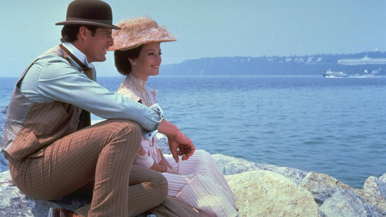 Richard and Elise sitting on rocks by lake in Somewhere in Time