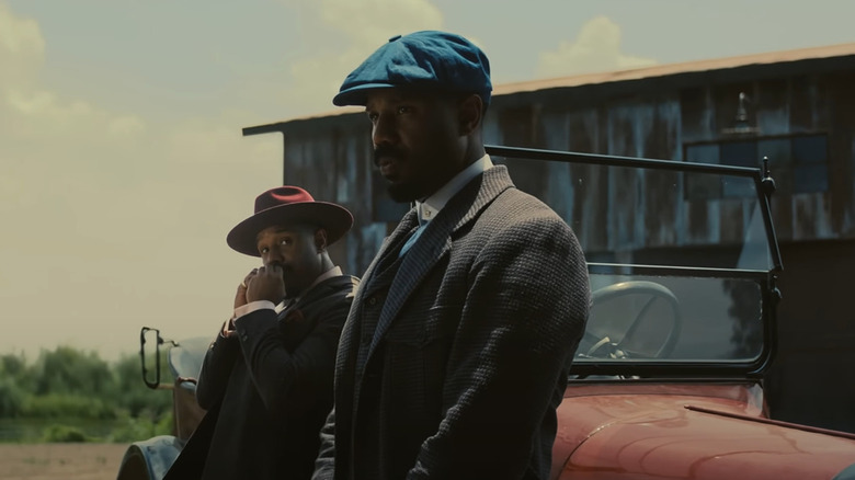 Smoke and Stack leaning on a car outside in "Sinners"