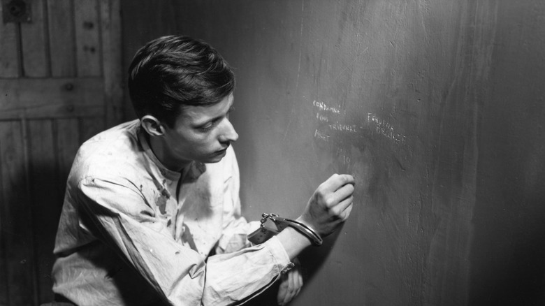Fontaine scratching words into the wall of his cell in A Man Escaped