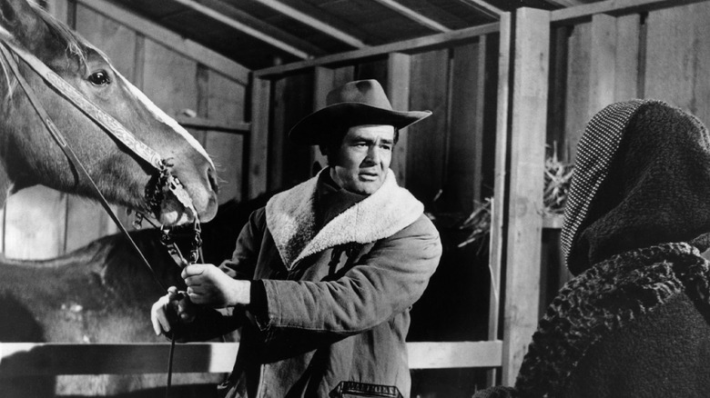 Blaise Starrett tending to a horse while looking at Helen Crane in Day of the Outlaw
