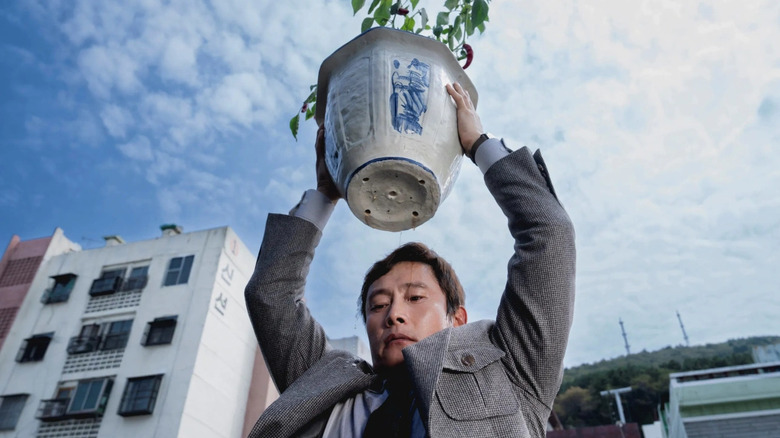Man-su lifts a potted plant in "No Other Choice" (2025)