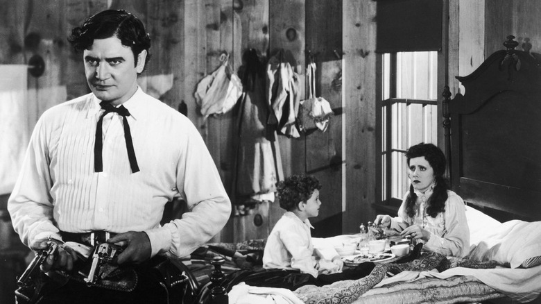 Yancey Cravat holds his guns in the bedroom with his family behind him in "Cimarron" (1931)