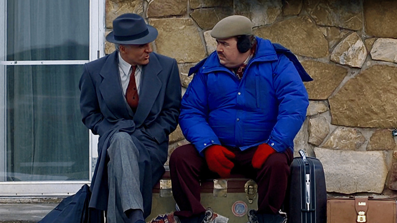 Neal and Del sitting on a bench in coats and talking in Planes Trains and Automobiles