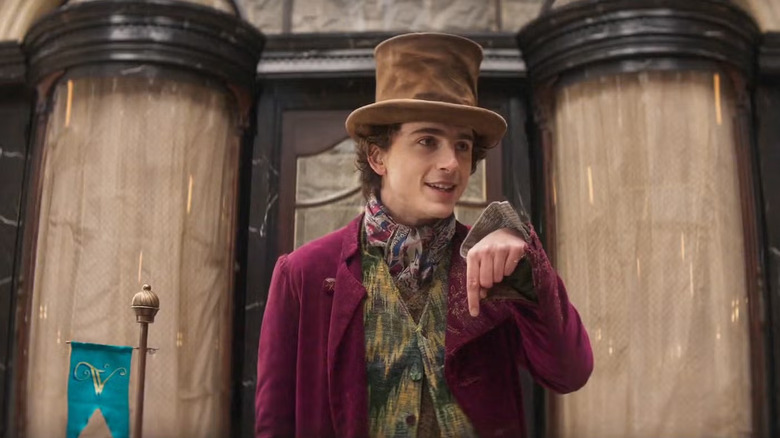 Wonka singing and pointing down in front of his hopeful chocolate shop in Wonka