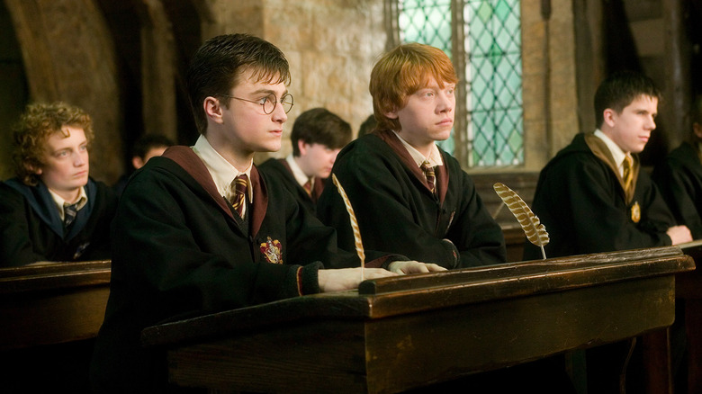 Harry and Ron sitting together in class at a dark, wooden desk with feather quills