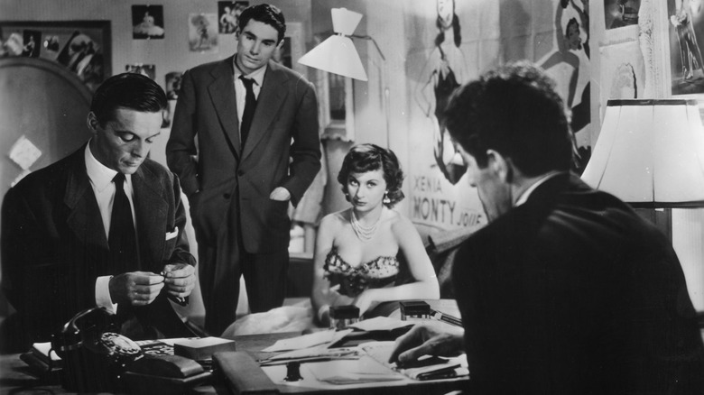 Two men in suits look down at a third man, while a woman in a dress sits nearby, in "Rififi"