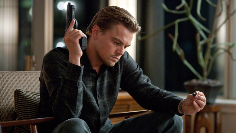 Dom Cobb holds a gun up next to his head, staring at a simple top, in "Inception" (2010)