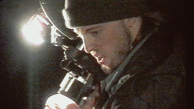 Michael holding a camera and looking down at something in "The Blair Witch Project" (1999)