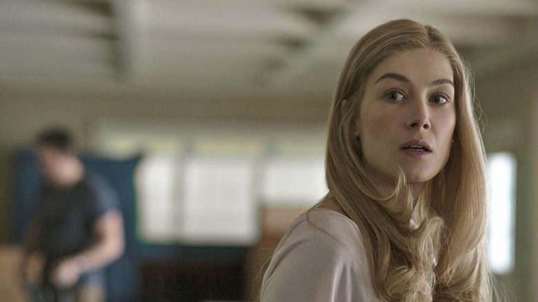 Amy looking over her shoulder with Nick in the background in Gone Girl