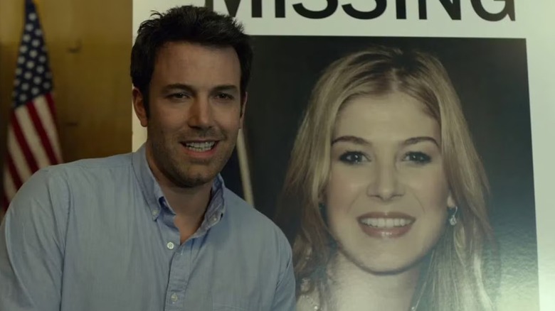 Nick Dunne smiling next to a "missing" poster of his wife in Gone Girl (2014)