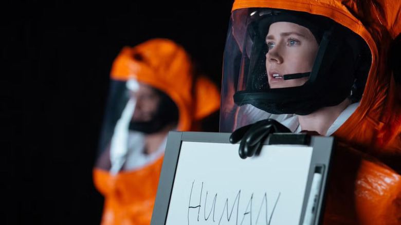 Louise in a suit holding up a whiteboard to the aliens in Arrival