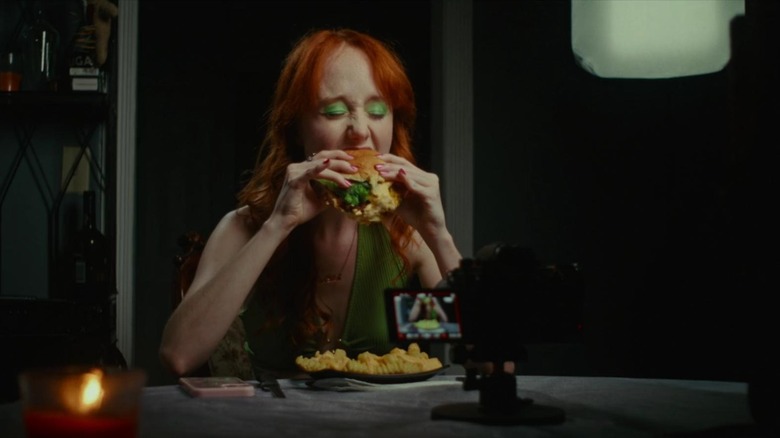 Ash chomping into a burger in Cannibal Mukbang (2023)