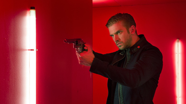 David aiming a revolver under red lights in The Guest (2014)
