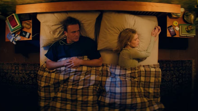 Dan and Lisa in bed wearing headphones in Over Your Dead Body