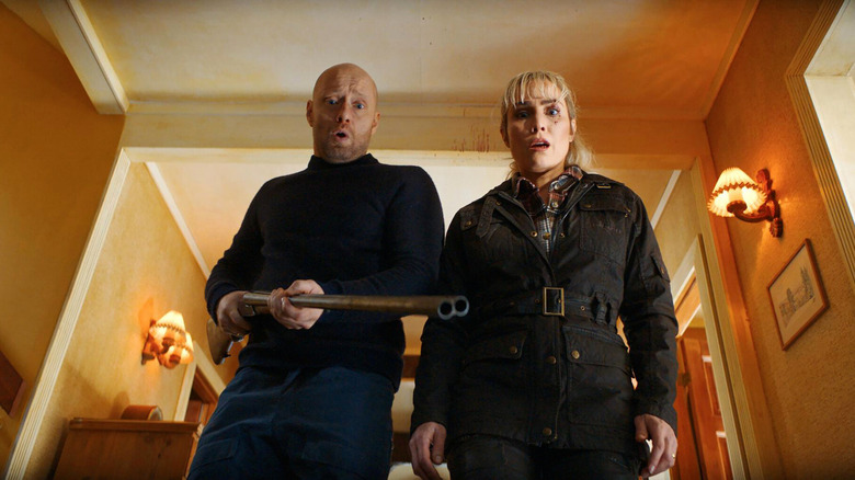 Lars holding a gun looking down at someone next to Lisa in The Trip