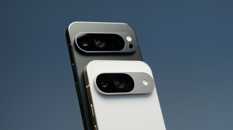 Two Google Pixel 9 phones and their rear camera visors with a black one standing atop a white one.