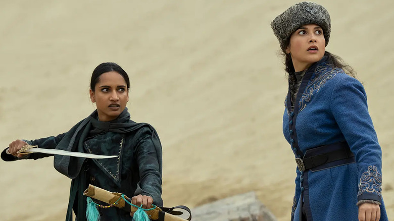Inej standing with her sword unsheathed and ready and Zoya (Sujaya Dasgupta) dressed in blue Grisha robes