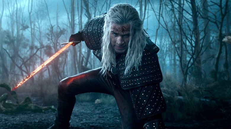 Geralt pulls his glowing sword in the forest in The Witcher