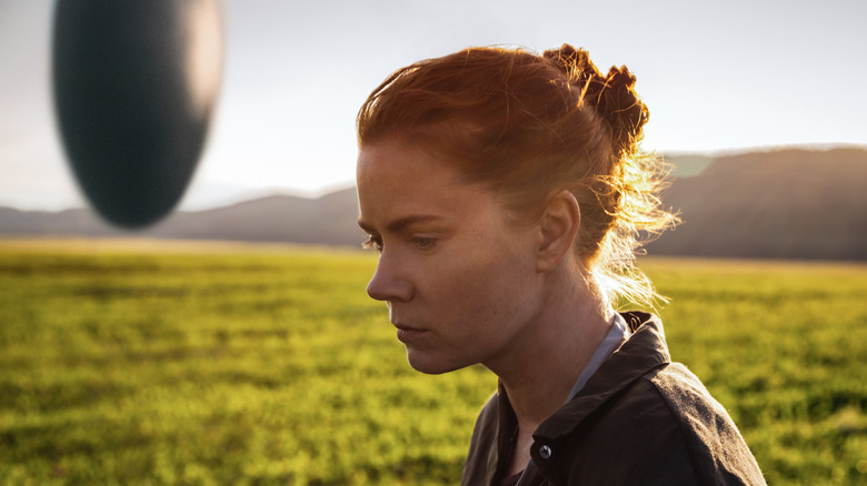 Louise Banks standing in a field with an alien ship floating in the background in "Arrival" (2016)