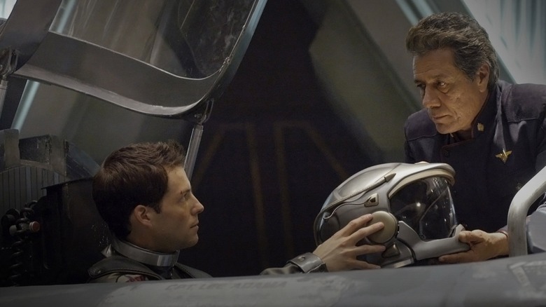 Cdr. William Adama handing a helmet to his son, Apollo, in "Battlestar Galactica" (2003-2009)