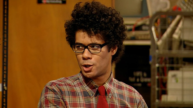 Maurice Moss wearing his signature short-sleeve button up with a tie and sitting in conversation in the IT department