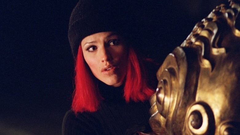 Sydney in a red wig and hat hiding behind a structure on Alias