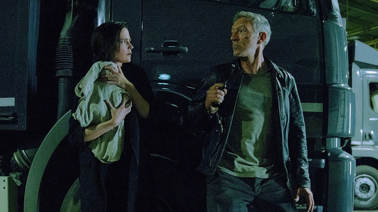 Rowdy holds a baby as she and Delage lean against a truck in Liaison (2023)