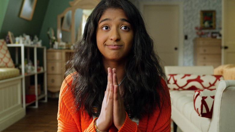 Devi praying in an orange sweater on Never Have I Ever