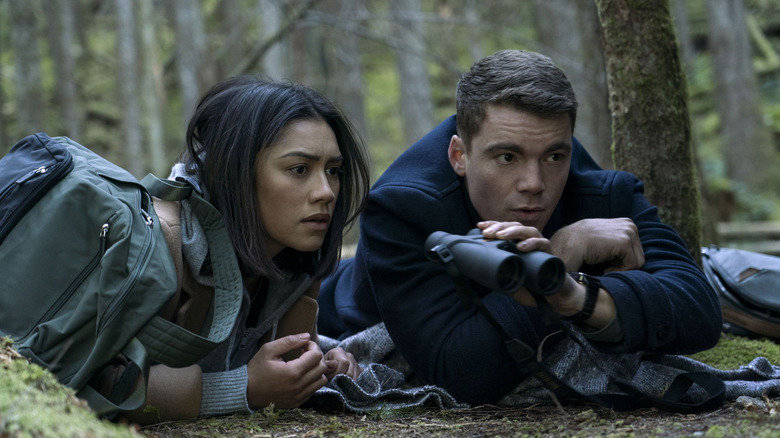 Rose and Peter in the woods with binoculars on The Night Agent