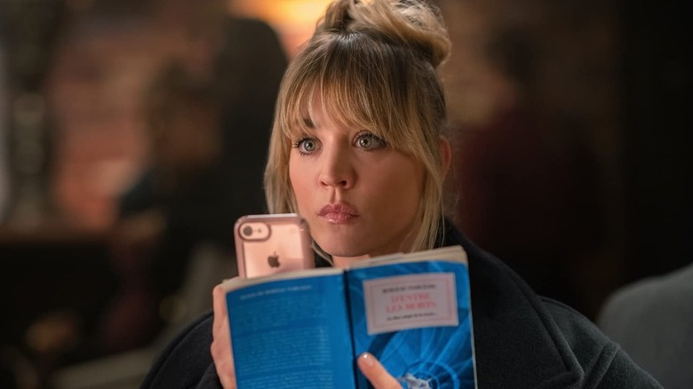 Cassie secretly recording with her phone behind a book in The Flight Attendant