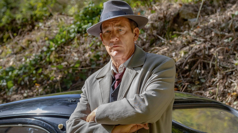 Spade crossing his arms and leaning against a car in "Monsieur Spade" (2024)
