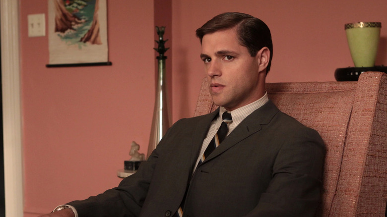 Greg sitting in a pink armchair looking dubious on Mad Men
