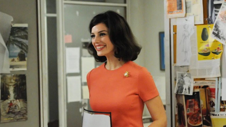 Megan smiling in an orange top in the SDCP office on Mad Men