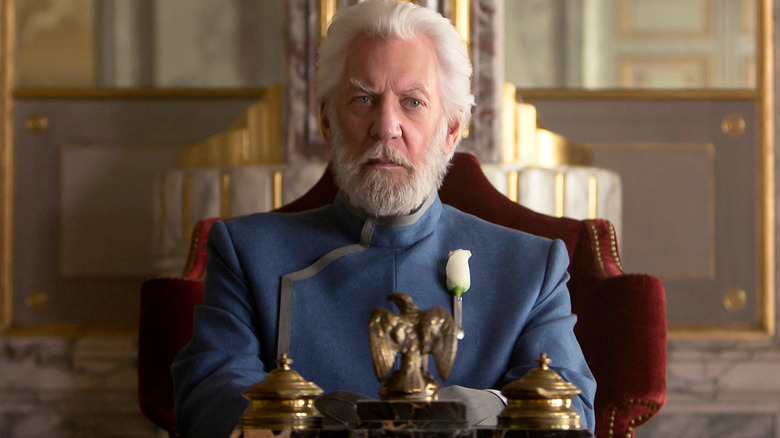 President Snow frowning at a table in "The Hunger Games"