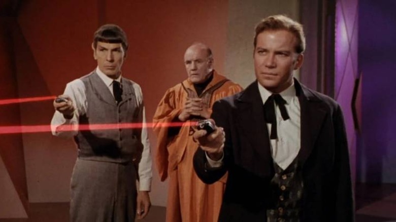 Spock and Captain Kirk firing phasers as a man watches in "Star Trek"