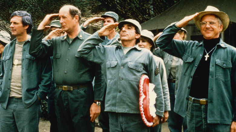 Hawkeye with his hands in his pockets as his colleagues salute in M*A*S*H
