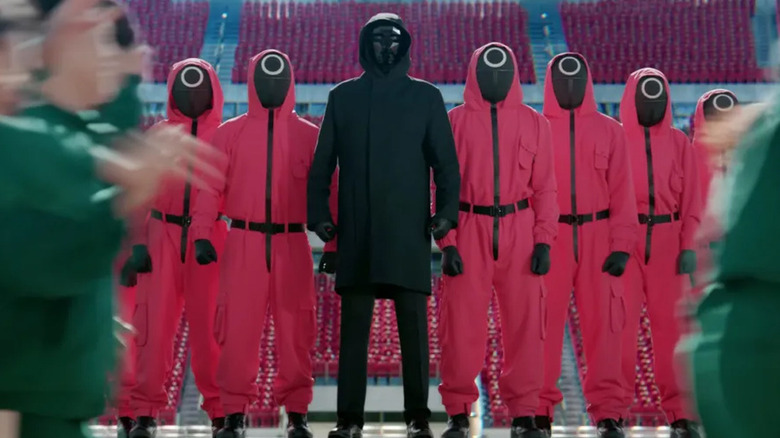 The Front Man and his pink-dressed, armed guards— all of whom are masked— stand in watch as a few blurs of contestants in green tracksuits participate in a game