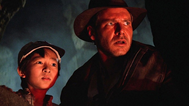 Short Round and Indiana Jones looking from behind the rocks in "Indiana Jones and the Temple of Doom"
