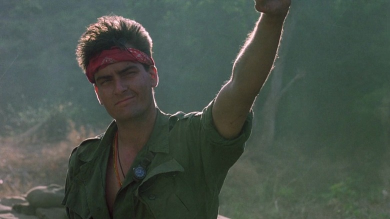 Charlie Sheen as Chris Taylor in "Platoon," a red bandana around his forehead, waving