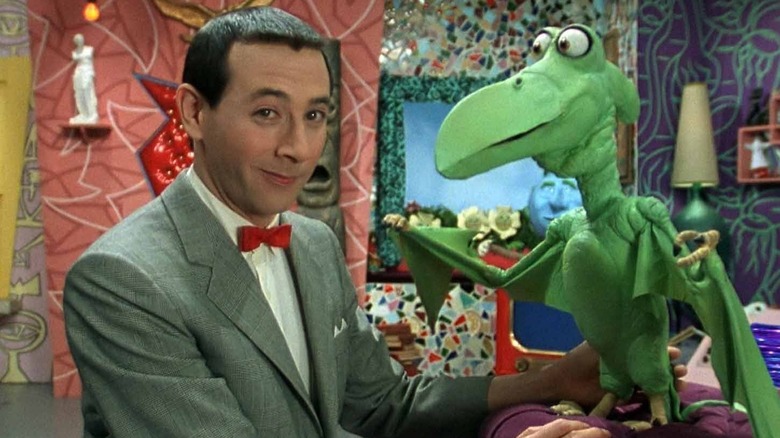 Pee-Wee Herman gives a wry smile in his playhouse next to a green puppet in Pee-Wee's Playhouse