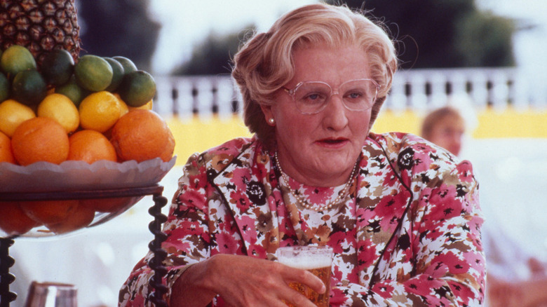 Mrs. Doubtfire sitting at an outdoor bar, drinking beer next to an elaborate bowl of citrus fruit