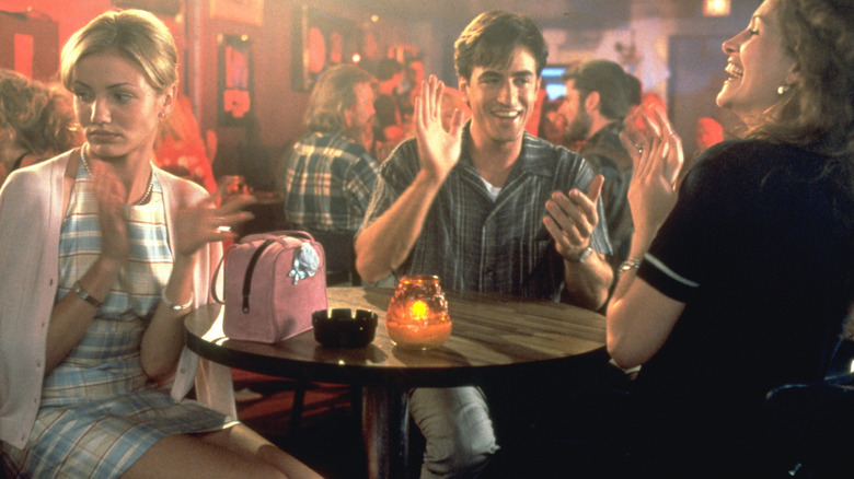Kimmy, Michael, and Julianne sitting at a small, round table and clapping for an off-camera karaoke performer