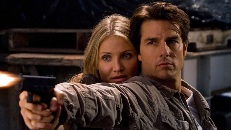 Roy pointing a gun with June hiding behind him in Knight and Day