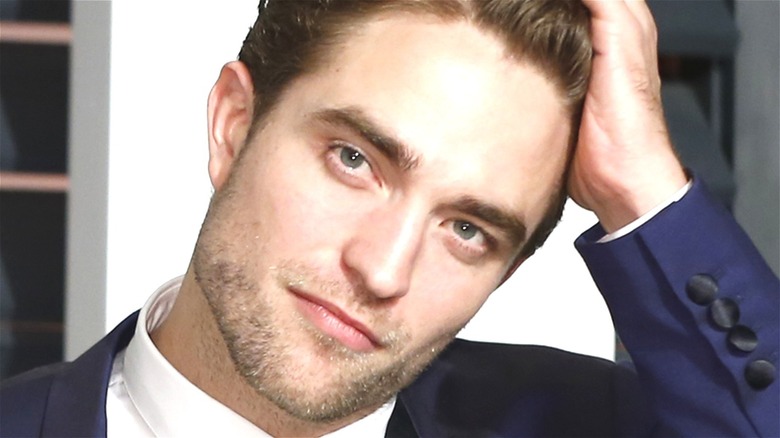 Robert Pattinson smiling and touching his hair